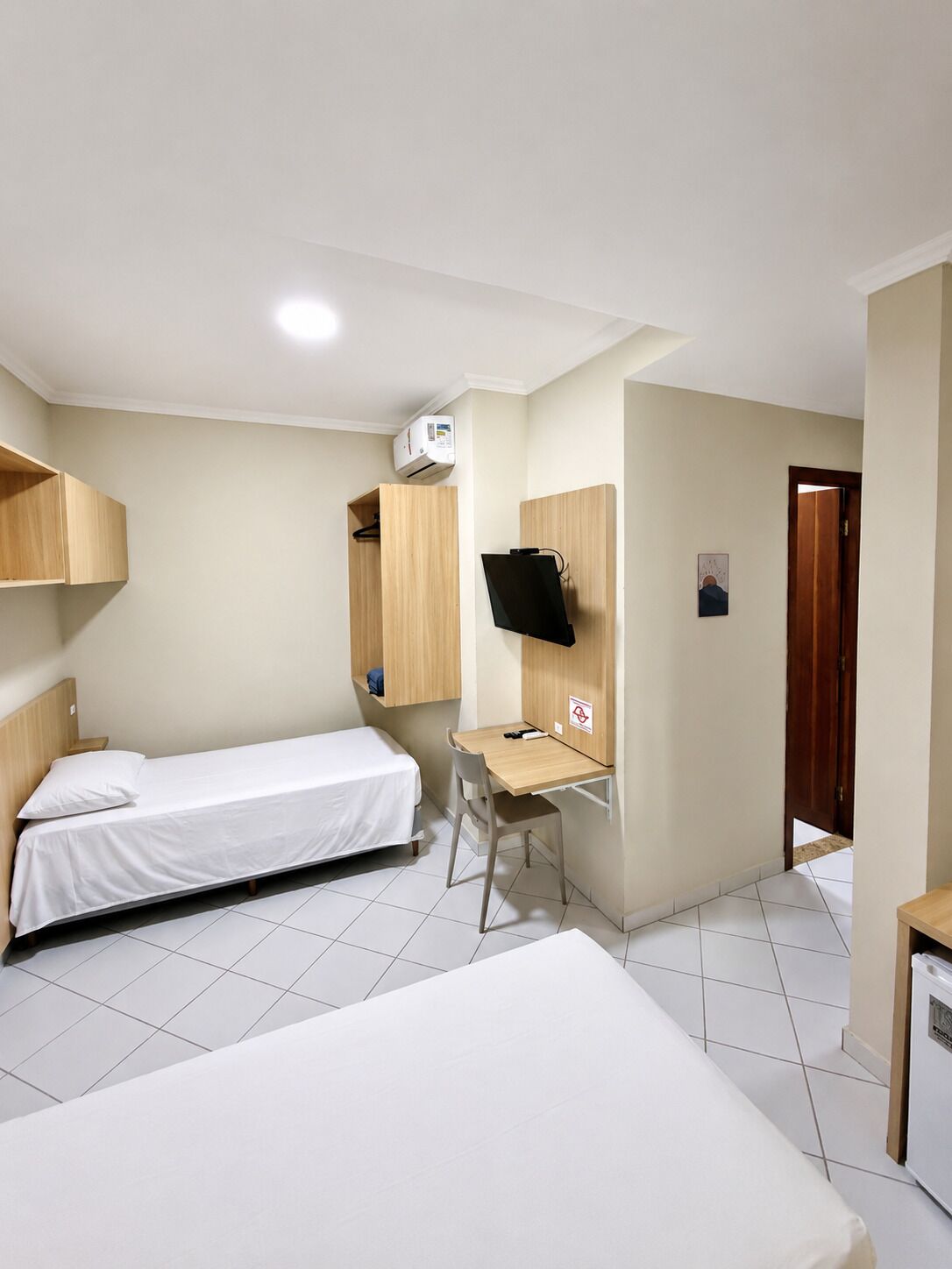 A hotel room with a bed, a desk, a chair, a television, and an air conditioning unit.