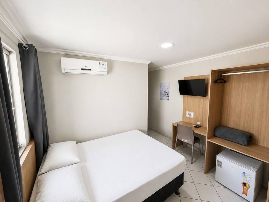Habitación de hotel con cama, escritorio, televisor, armario y mini refrigerador.