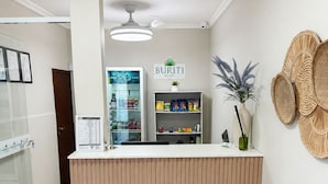 Un mostrador de recepción con un letrero que dice 'BURITI HOTEL', una vitrina con aperitivos, una cesta tejida colgada en la pared y un área de recepción con un banco de madera.