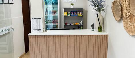 Un mostrador de recepción con un letrero que dice 'BURITI HOTEL', una vitrina con aperitivos, una cesta tejida colgada en la pared y un área de recepción con un banco de madera.