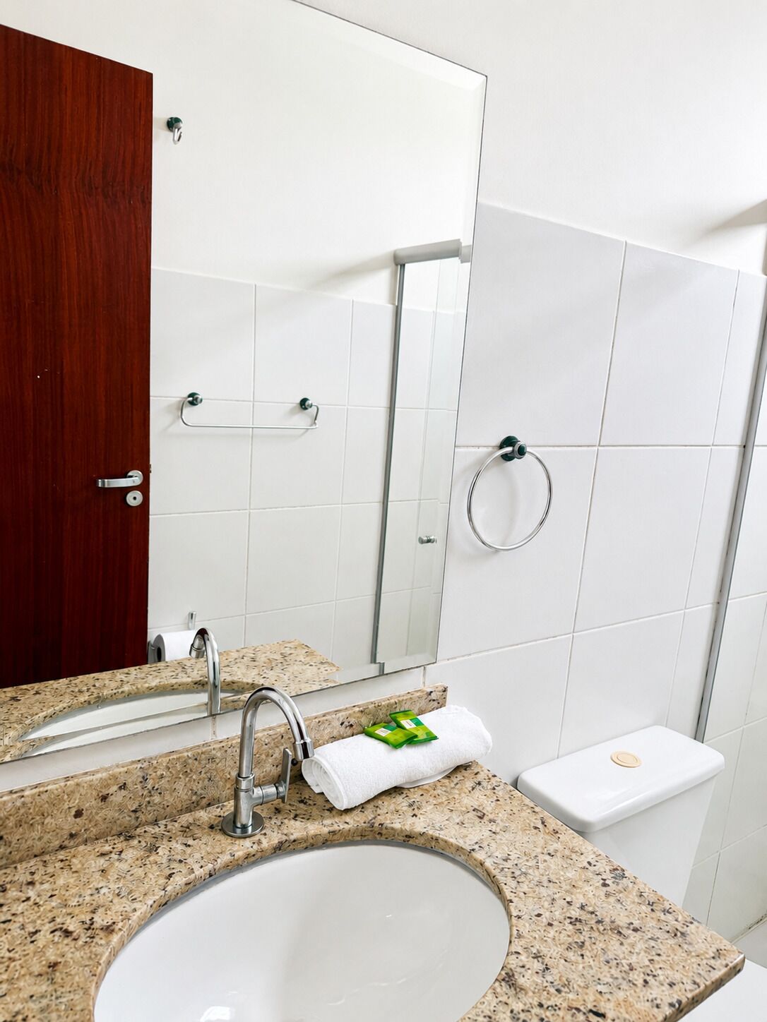 A bathroom with a granite countertop sink, a mirror, a towel rack, and a toilet.