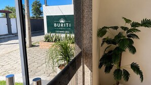 Entrada de hotel con un cartel que dice 'BURITI HOTEL', una planta en maceta y una reja metálica.