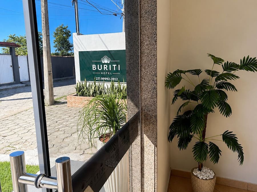 Entrada de hotel con un cartel que dice 'BURITI HOTEL', una planta en maceta y una reja metálica.