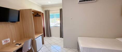 Une chambre d’hôtel équipée d’un lit, d’un bureau avec une chaise, d’un téléviseur fixé au mur et d’un appareil de climatisation.