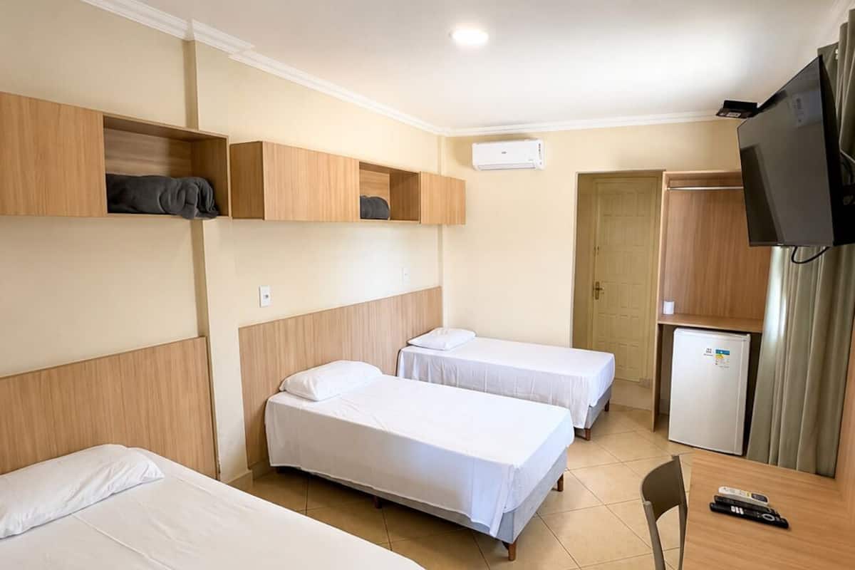 A hotel room with two single beds, a desk, a chair, a television, and a mini-fridge.