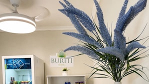 Zona de recepción de hotel con un refrigerador lleno de bebidas, un panel con la carta, un jarrón con plantas decorativas y un letrero del hotel.