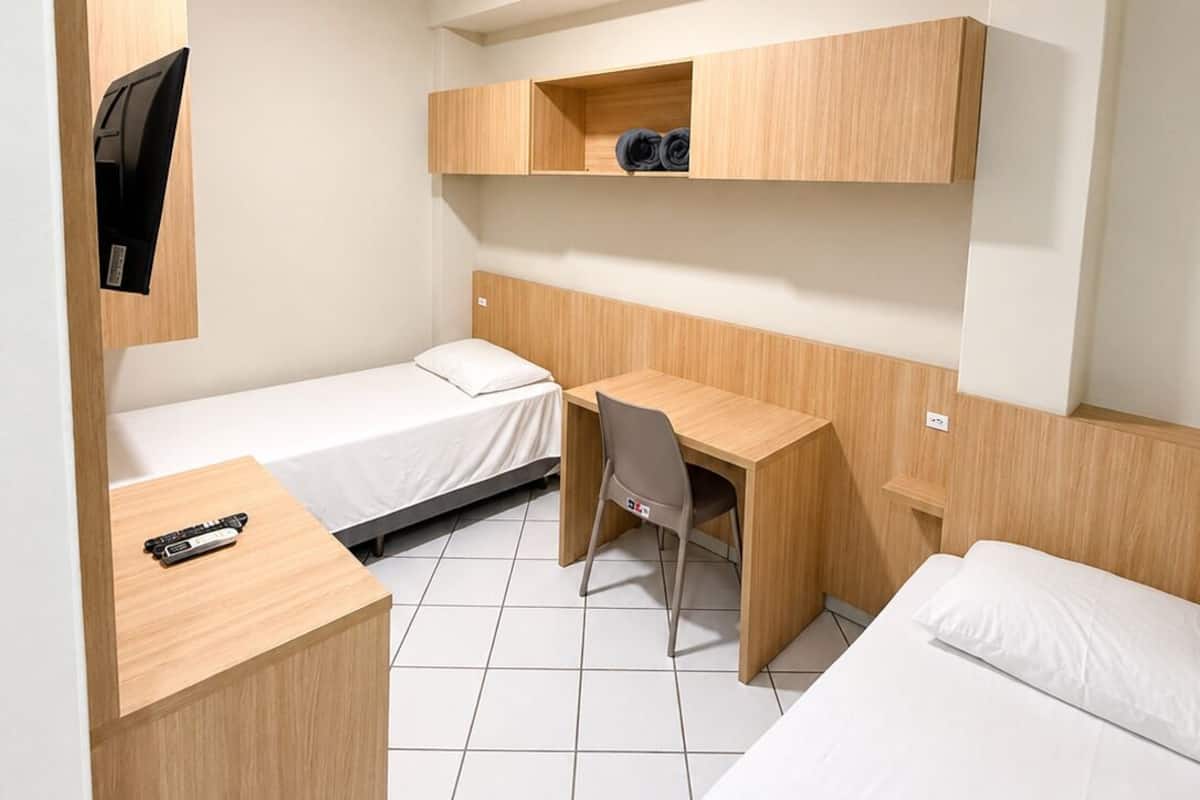 A compact hotel room with a bed, a desk, a chair, and a TV.