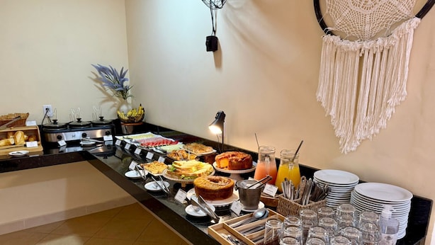 Un bufé con diferentes alimentos, una cesta de frutas y un tapiz de macramé en la pared.