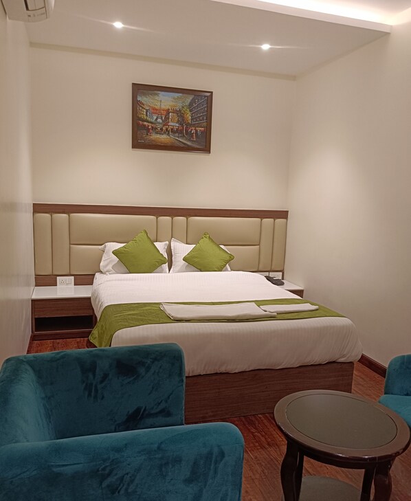 A hotel room with a bed, two green chairs, a small table, and a painting on the wall. - The Pride (Golmuri)