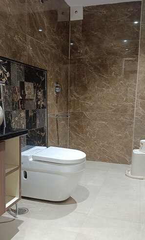 A modern bathroom with a white toilet, a black vanity with a mirror, and a shower area with a glass door. - The Pride (Golmuri)