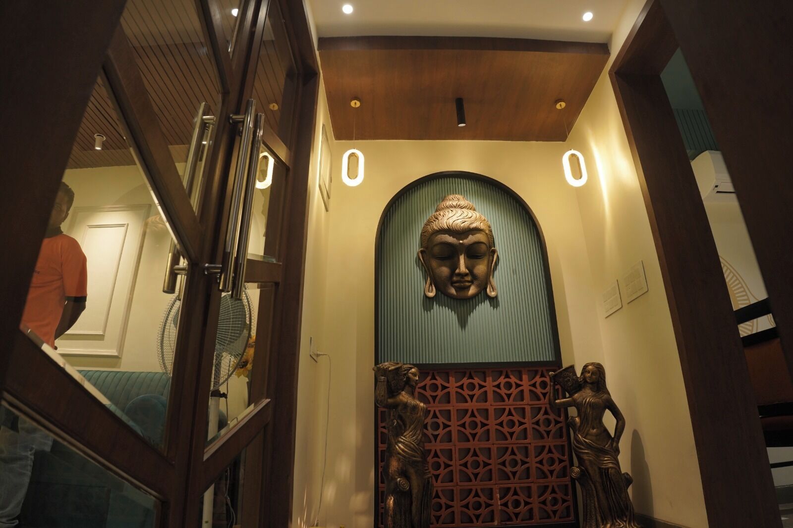 A hallway with a Buddha statue, a fan, and a decorative screen.