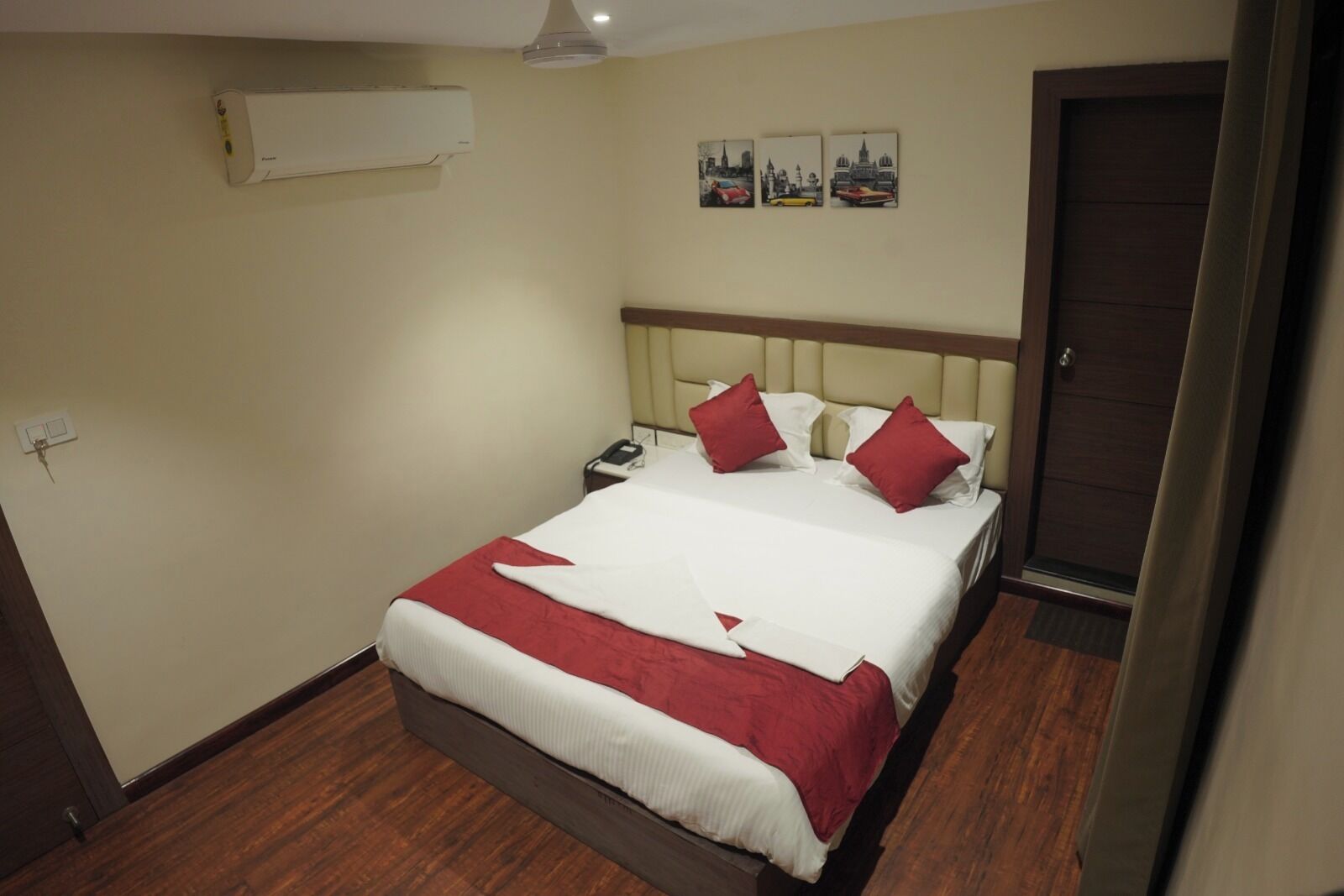 A hotel room with a bed, a nightstand, an air conditioning unit, and a door.