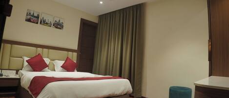 A hotel room with a bed, a desk, a chair, a ceiling fan, and a window with curtains.