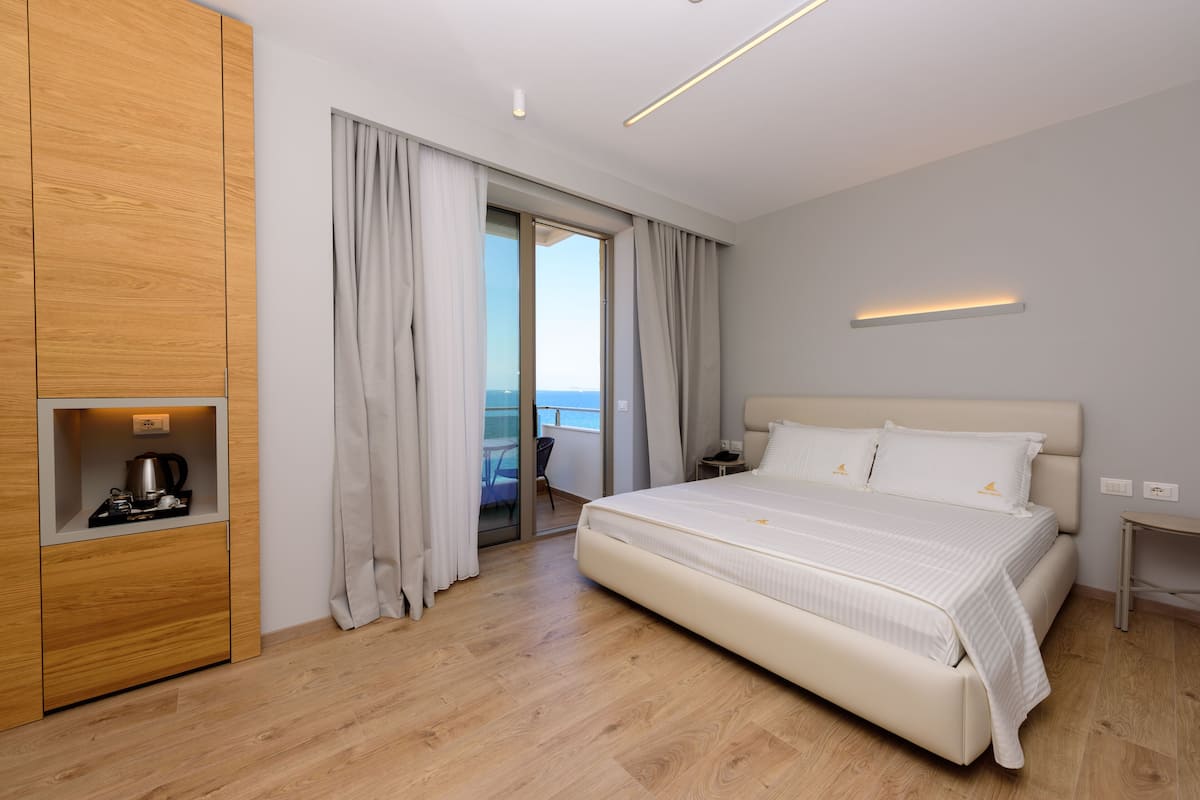 Une chambre d’hôtel moderne avec un grand lit, une armoire en bois et une vue sur la mer depuis le balcon.