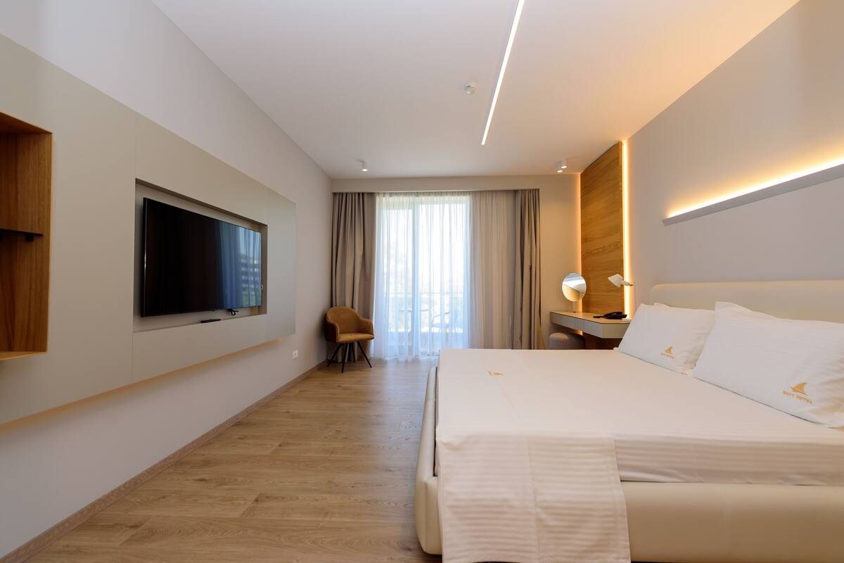 Une chambre d’hôtel moderne dotée d’un grand lit, d’un téléviseur à écran plat fixé au mur, d’un bureau avec une lampe et d’une chaise.