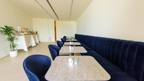 Un comedor moderno con una fila de mesas y sillas azules, un sofá azul oscuro y una planta en maceta.