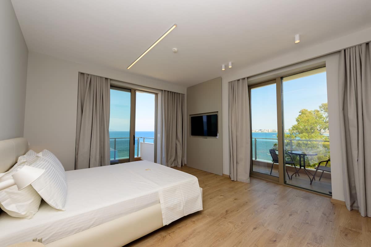 Une chambre d’hôtel moderne dotée d’un grand lit, d’une télévision et d’un balcon offrant une vue sur la mer.