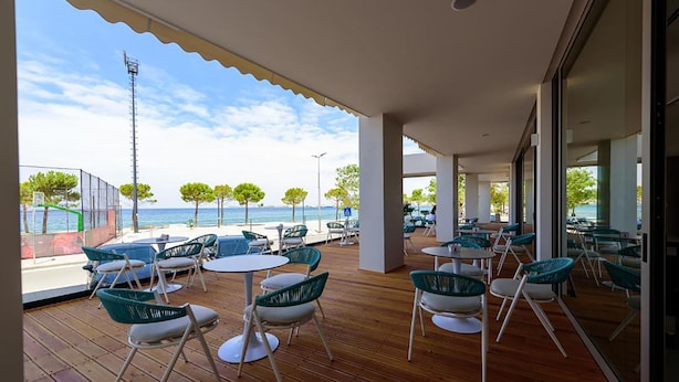 Un espacio al aire libre con mesas y sillas, con vista a una playa y al mar.