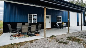 A building with a blue exterior, a covered patio with outdoor furniture, and a garage door. - New Rustic Retreat, Firepit & Games, Hiking, Boating & Fishing near Lake Rathbun (Moravia)