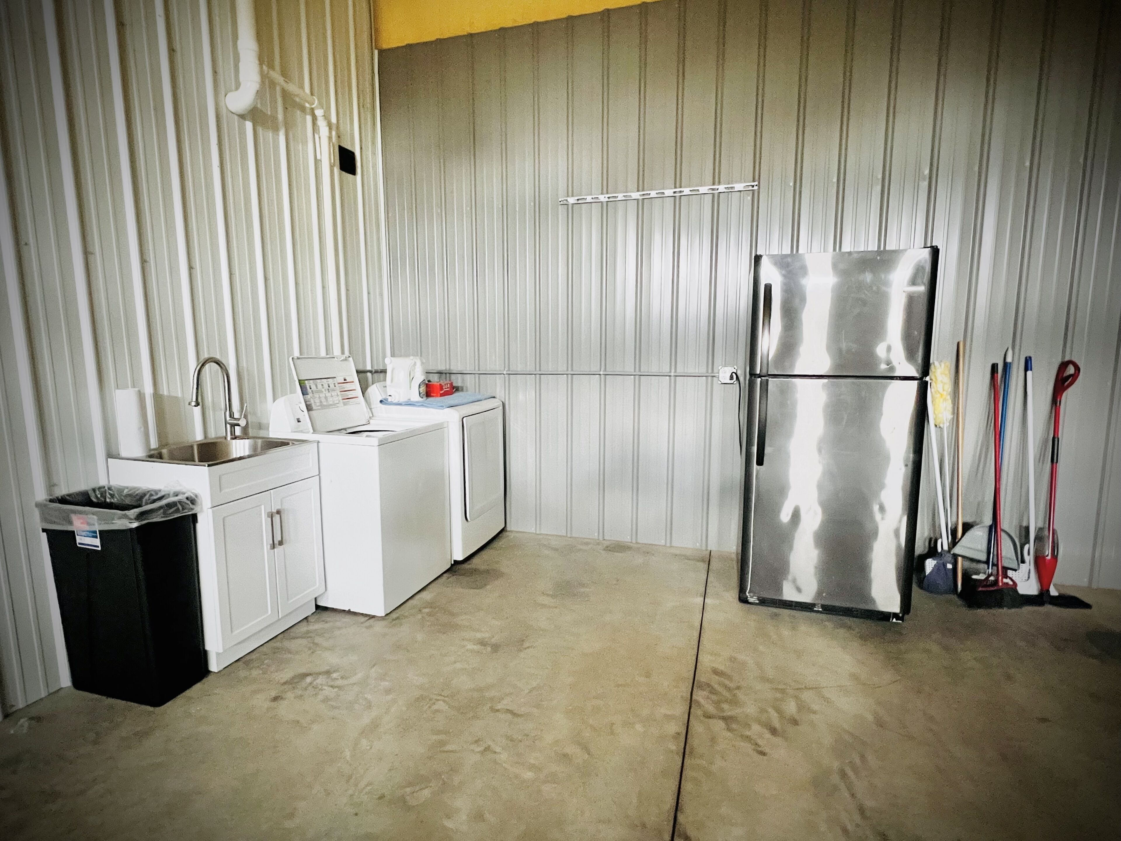 A compact kitchen with a stainless steel refrigerator, a washing machine, and a sink.