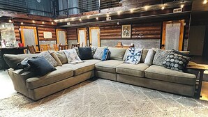 A cozy, log cabin-style room with a large sectional sofa, a ceiling fan, and a 'Phillips 66' neon sign. - New Rustic Retreat, Firepit & Games, Hiking, Boating & Fishing near Lake Rathbun (Moravia)