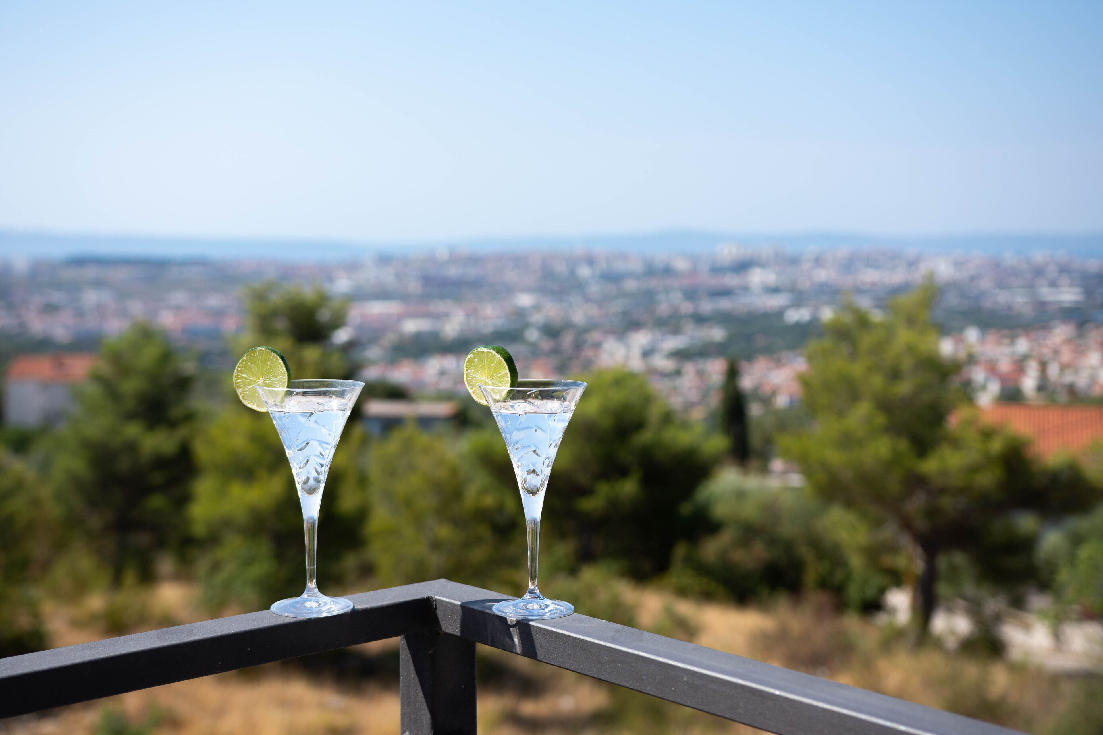 Dos copas de martini en un balcón con vista a un paisaje urbano.