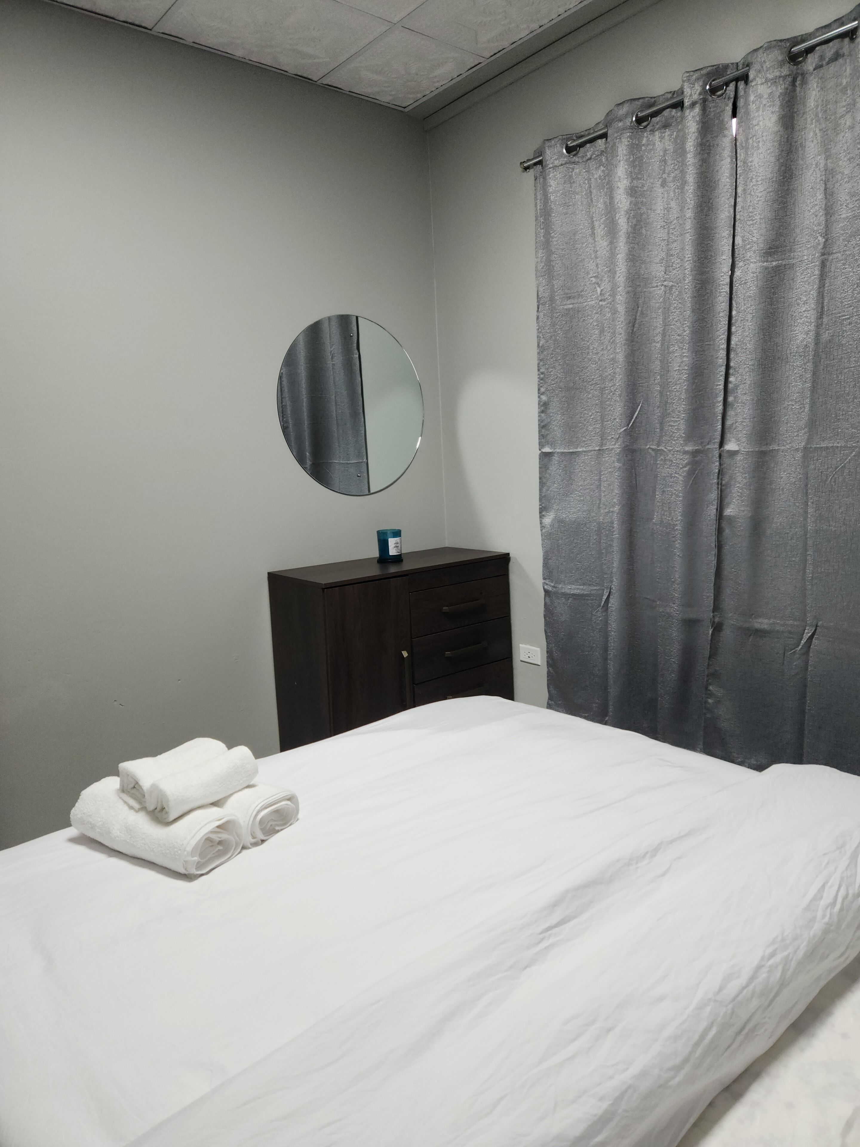 Une chambre à coucher avec un lit, une commode, un miroir et une fenêtre avec des rideaux.