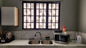 Une cuisine équipée d’un évier à deux bacs, d’un four à micro-ondes, d’une bouilloire et d’une fenêtre avec des stores à motifs floraux.