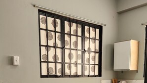 Une petite pièce propre, avec un sol carrelé, deux fauteuils en osier, une petite table ronde, une fenêtre avec des stores décoratifs, un meuble et un four à micro-ondes.