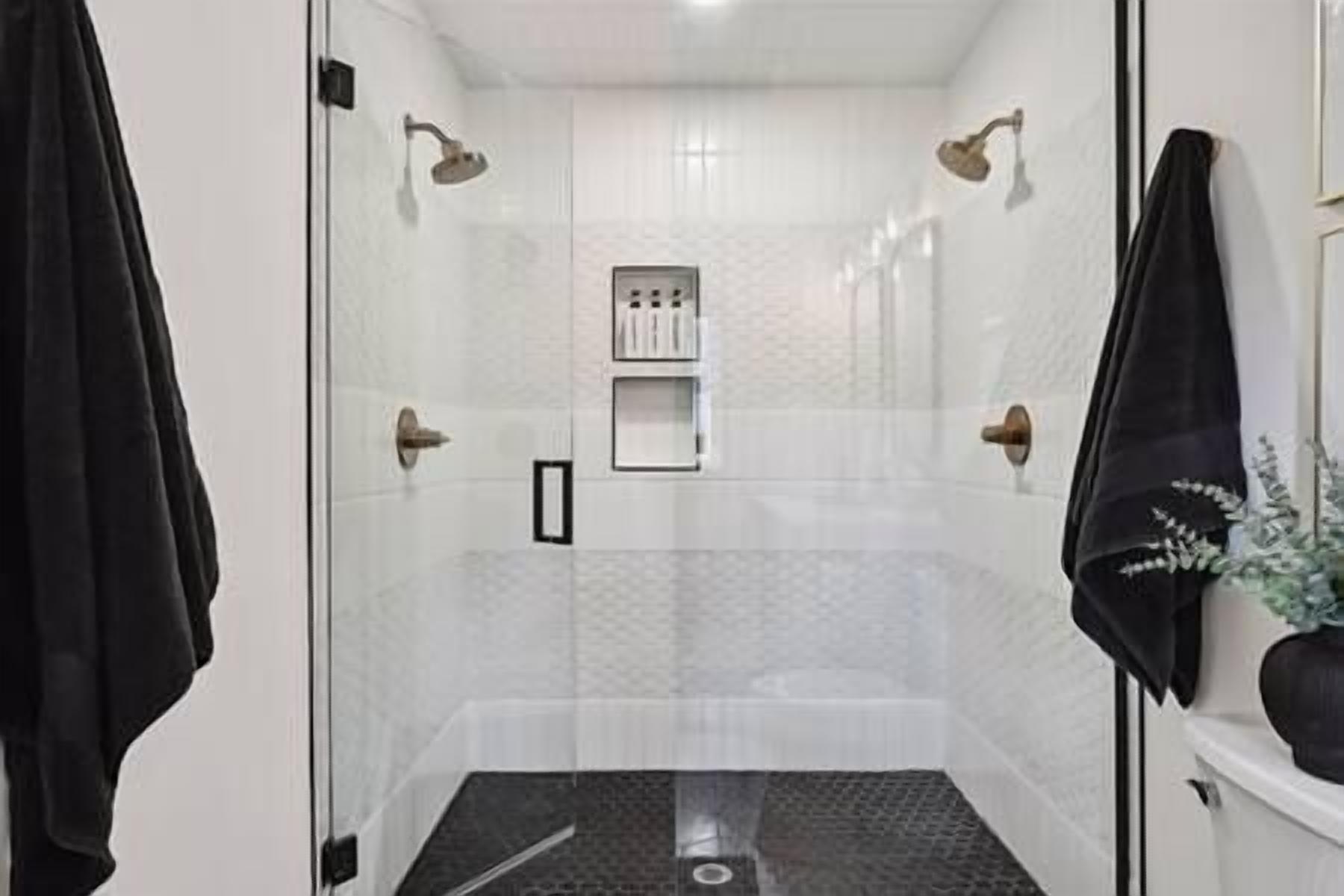 A glass-enclosed shower with a tiled floor, a control panel, and a towel rack.