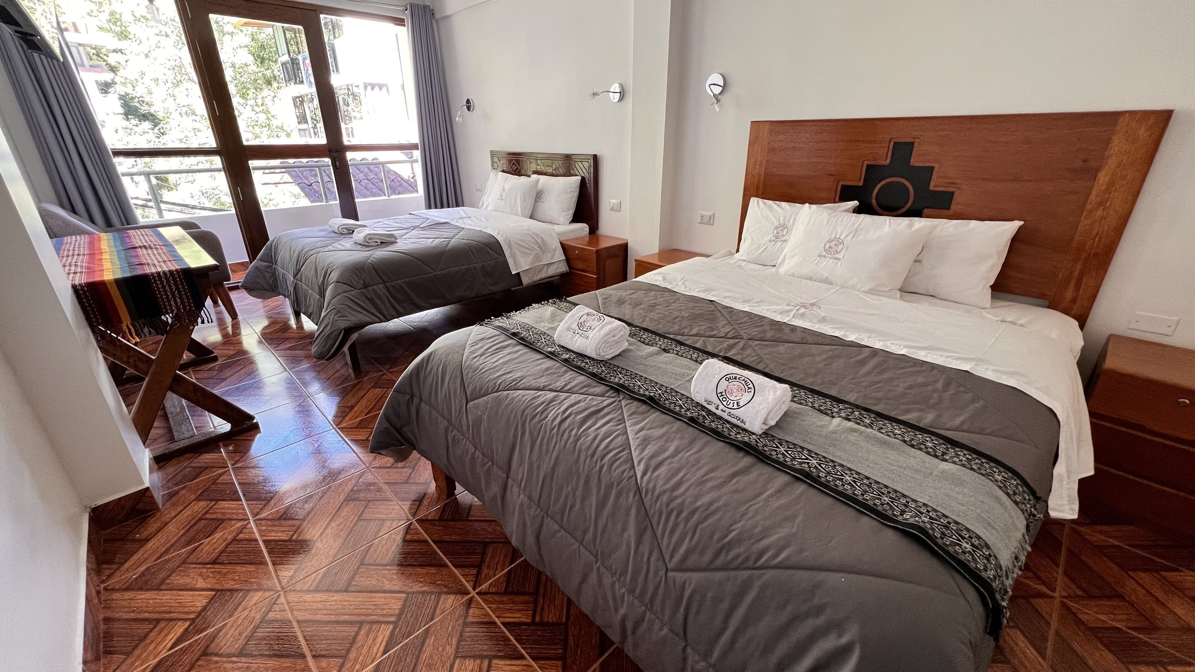 A hotel room with two beds, a wooden floor, and a view of the outside through a large window.