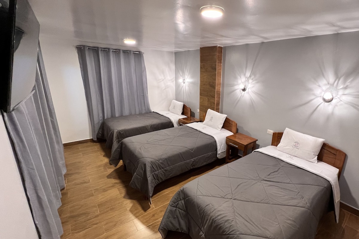 A hotel room with two single beds, wooden headboards, grey bedding, a wooden floor, and a grey curtain.