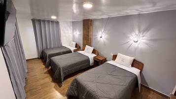 A hotel room with two single beds, wooden headboards, grey bedding, a wooden floor, and a grey curtain.