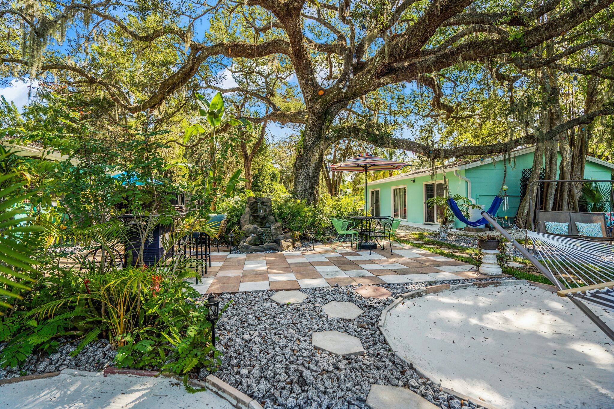 A tropical garden with a hammock, outdoor seating, and a checkered patio.