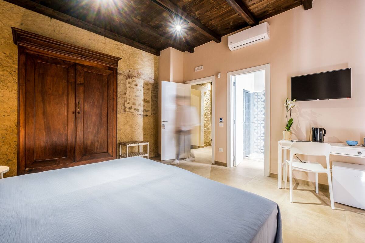 A hotel room with a bed, a desk, a chair, a TV, and a wardrobe.