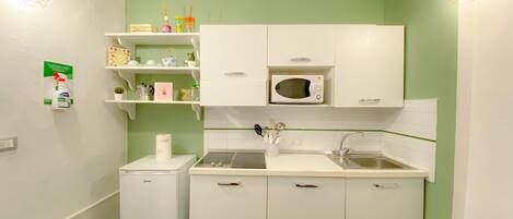 A compact kitchen with white cabinets, a microwave, a sink, and a small refrigerator.