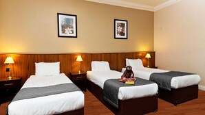 Une chambre d’hôtel avec trois lits simples, des têtes de lit en bois et des lampes de chevet.