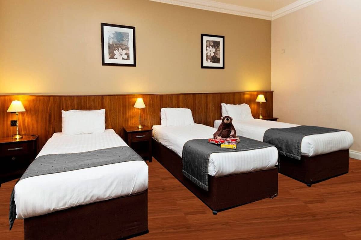 Habitación de hotel con tres camas individuales, cabeceras de madera y lámparas de noche.