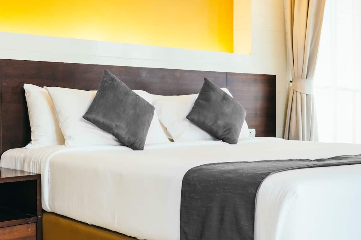 Una cama bien hecha con almohadas blancas y gris oscuro, un cabecero de madera y una mesita de noche con una lámpara.