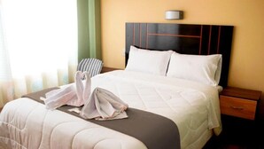 Un lit bien fait, recouvert d’une courtepointe, une table de chevet avec un tiroir et une lampe fixée au mur.