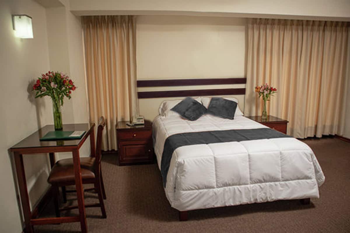 Habitación de hotel con una cama individual, un escritorio con silla, una mesita de noche y dos jarrones de flores.