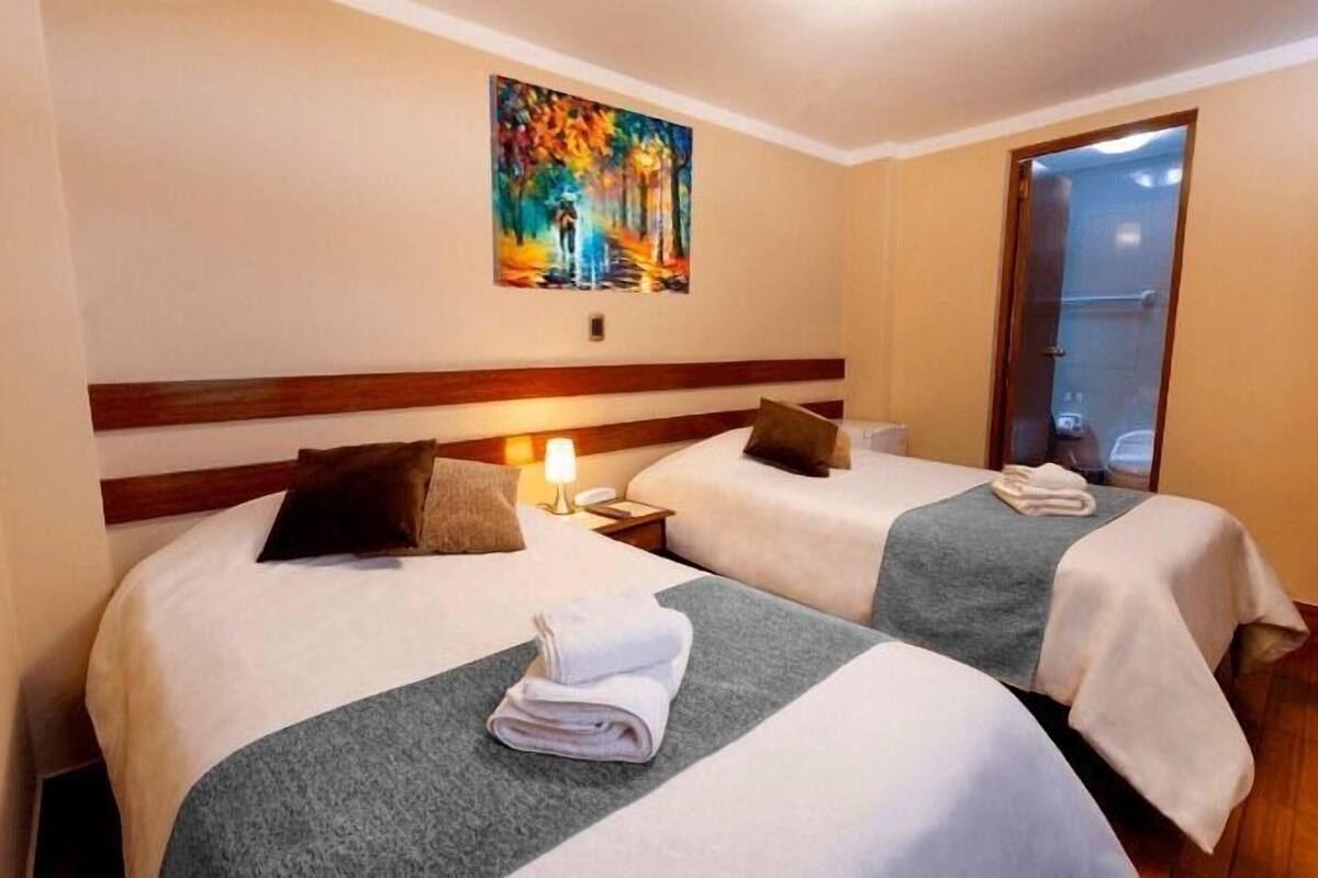 Habitación de hotel con dos camas, un cuadro en la pared y una puerta que da a un baño.