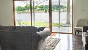 A living room with a gray sofa, a chair, and a view of a lake through large glass doors. - Chesapeake City Quiet Overlook (Chesapeake City)