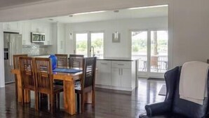 A spacious living area with a wooden dining table and chairs, a kitchen with white cabinets, and a balcony with a view. - Chesapeake City Quiet Overlook (Chesapeake City)