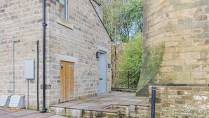A stone building with a wooden door and a small set of steps leading to a gated entrance. - 1 bedroom accommodation in Haworth (Haworth)