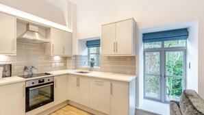 A modern kitchen with white cabinetry, a built-in oven, and a window with blue curtains. - 1 bedroom accommodation in Haworth (Haworth)