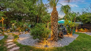 Un jardín con un sendero de piedra, palmeras y un pabellón.