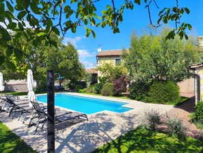 Una piscina con sillas de descanso, rodeada de vegetación y una casa al fondo.