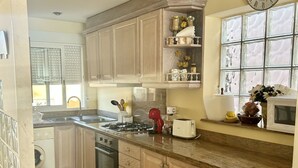 A kitchen with wooden cabinets, a gas stove, a microwave, and a clock on the wall. - Sea Beach House (Oliva)