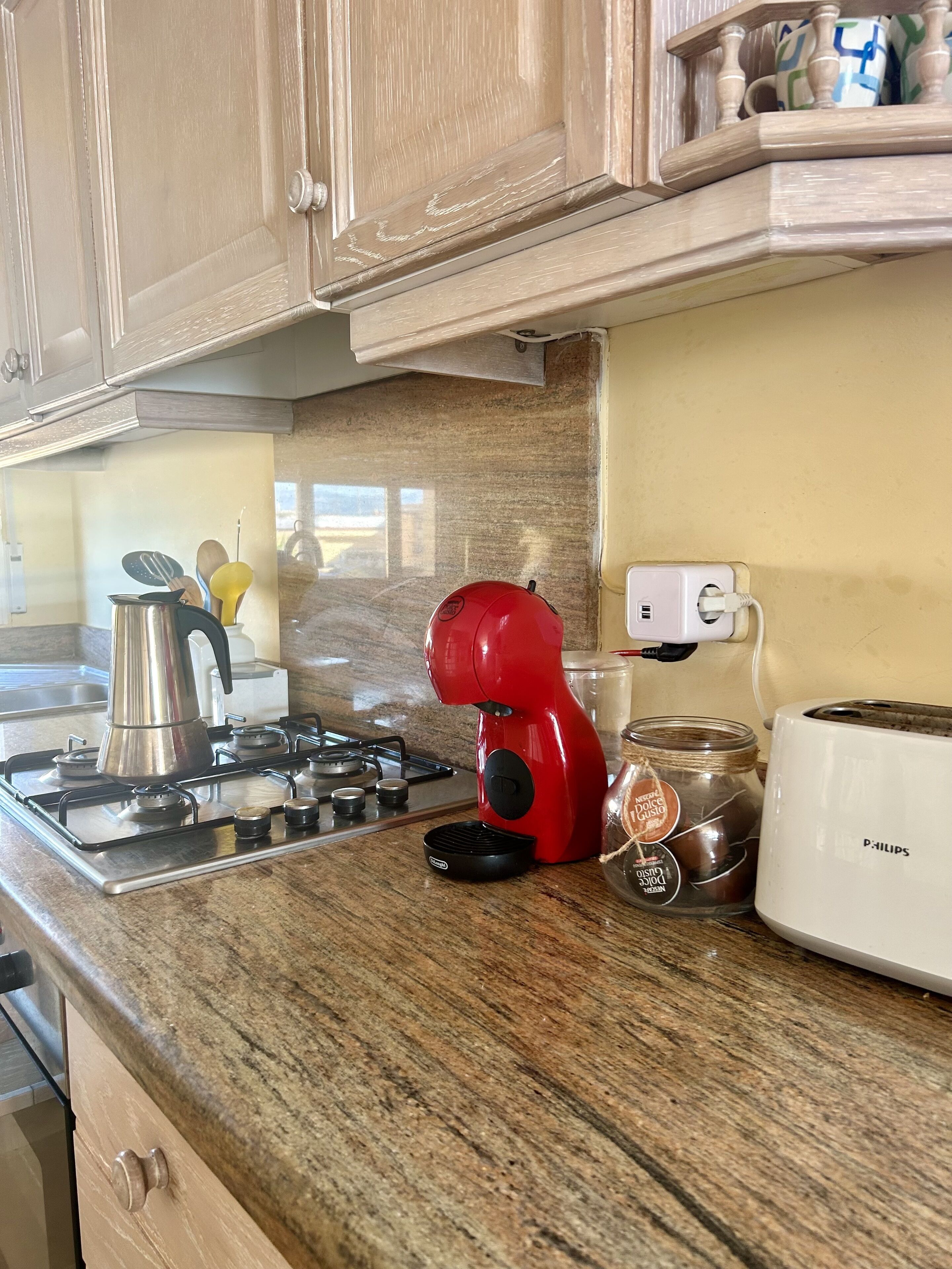 A kitchen with a gas stove, a red coffee maker, a jar of coffee, and a white toaster.